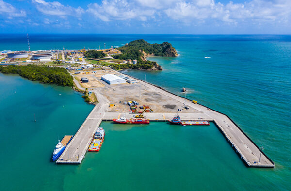 NGC | An aerial view of a small harbor with several boats docked at the piers. The harbor is surrounded by clear blue water and coastline with buildings and greenery in the background.