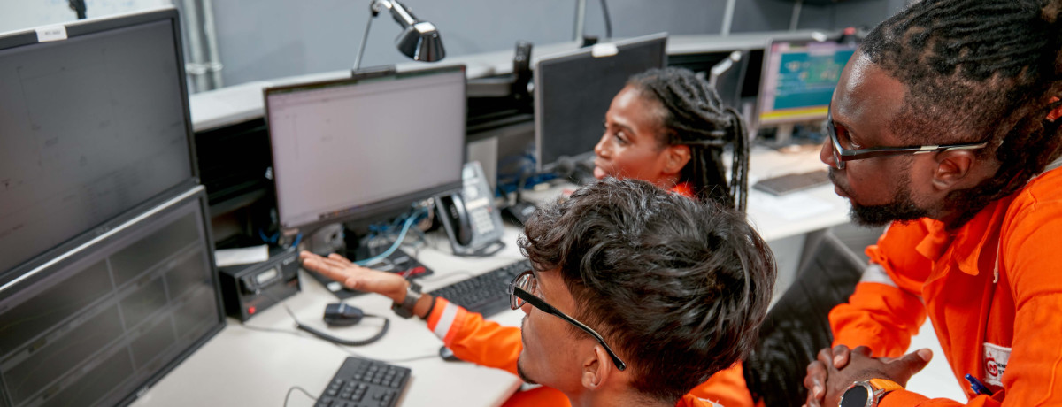 NGC | Three people in orange uniforms are engaged in core business activities at computer workstations, surrounded by multiple monitors in an office setting.