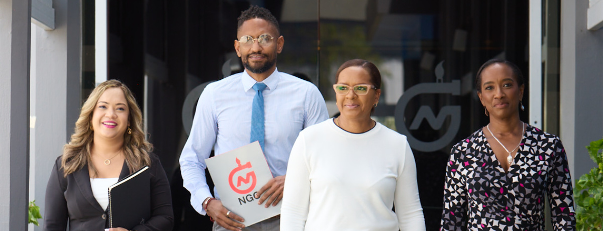 NGC | Four people standing outdoors in front of a building entrance, smiling and holding folders, radiate enthusiasm for new career opportunities.