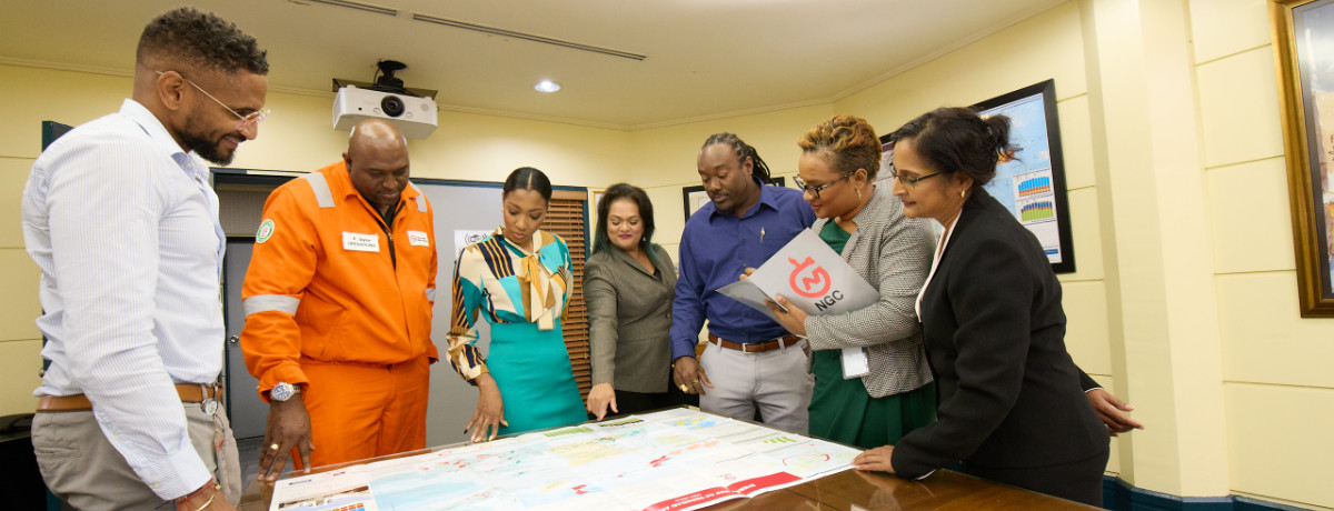 NGC | A group of people stands around a table in a conference room, analyzing the map-like layout of a financial performance document.