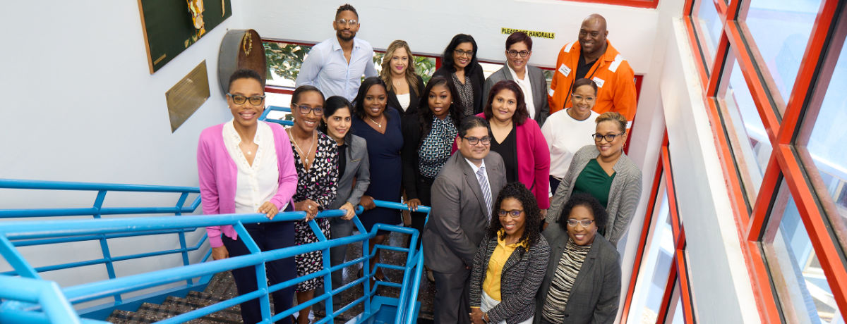 NGC | A group of 16 individuals posed on a staircase indoors, exuding professionalism as they stand or sit in business attire. The "Fire Exit Only" sign subtly highlights their commitment to safety and governance in the workplace.