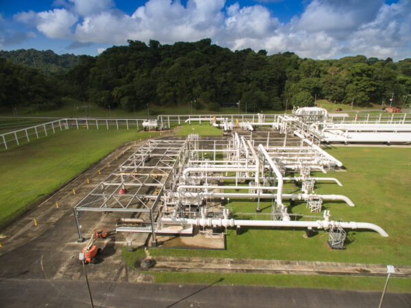 NGC | Aerial view of an industrial gas pipeline facility with white pipes and equipment set in a green landscape, bordered by a forest.
