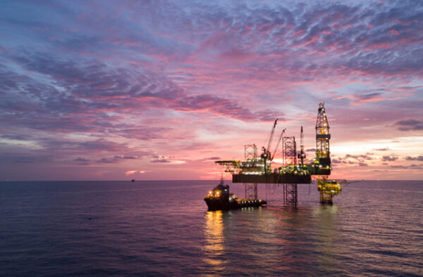 NGC | Offshore oil rig and support vessel in the ocean at sunset, with a colorful sky and calm water.