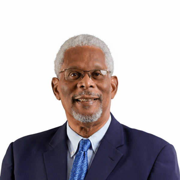 NGC | An older man with gray hair, a beard, and glasses wears a navy suit, light blue shirt, and blue patterned tie, posing in front of a plain white background—perfect for a professional Board of Directors profile.